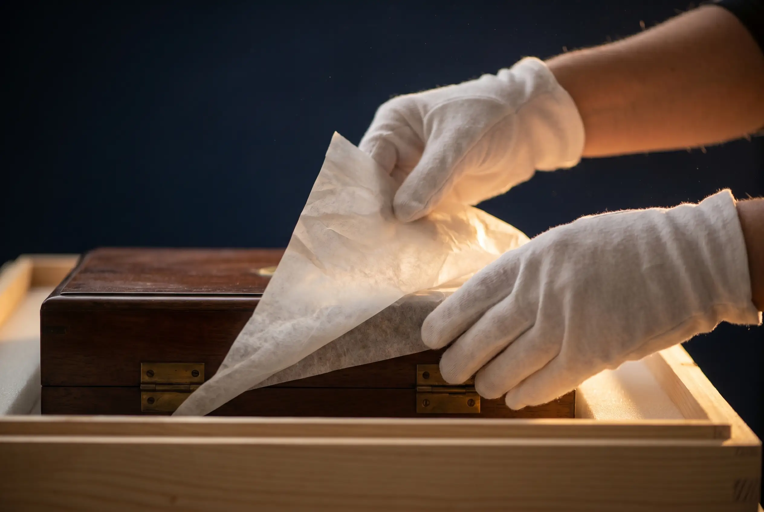 Gloved hands laying acid-free tissue over an antique inside a custom-built wooden crate